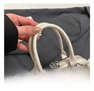 Close-up of cream faux leather shell bag with reinforced dual handles and silver hardware
