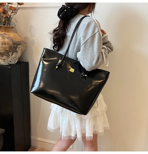 Detail view of glossy black tote bag with gold metal plate and knotted leather strap