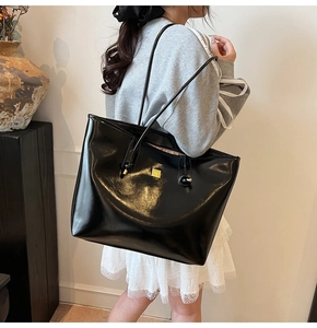 Close-up of a large black patent leather tote bag with gold hardware and slim straps