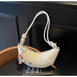 Détail du sac demi-lune en cuir blanc avec sangle à nœuds et pendentif de poupée