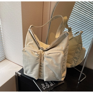 Detail of a large cream nylon tote bag with functional front zip pockets and wide strap