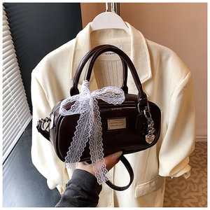 Detail of chocolate brown glossy leather bowling bag with lace bow and heart charm pendant