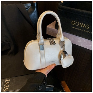 Close-up of cream shell handbag with heart charm and textured faux leather details