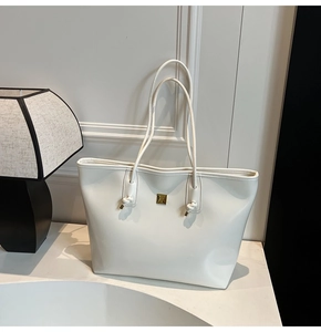 Detail of white glossy tote bag with golden logo and unique knotted strap design
