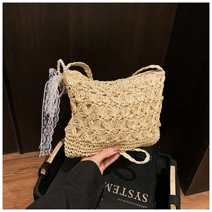 Detail der beigen Strohtasche mit Perlenriemen und weißer Schleife für den Sommer