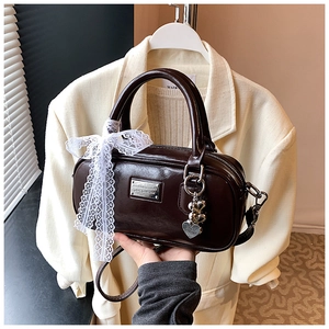 Detail of a dark brown bowling bag with white lace bow and heart-shaped metal charm