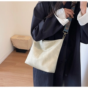 Detail of light beige bucket bag with ethnic style woven wide shoulder strap and gold hardware