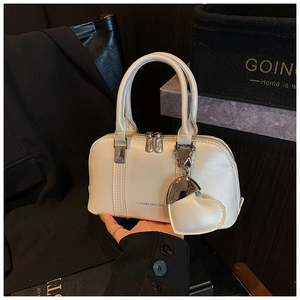 Close-up of white Boston handbag with silver hardware and heart-shaped pendant accessory
