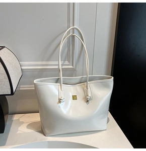 Close-up of white tote bag featuring a polished gold metal logo and smooth leather texture