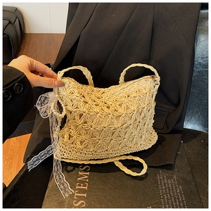 Detail der beigefarbenen Strohtasche mit floralem Lochmuster und Perlen-Spitzenanhänger