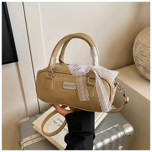 Close-up of khaki bowling bag with metallic logo plate and white lace bow detail