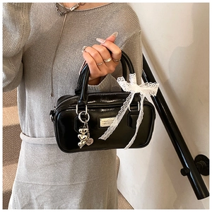 Detail of black glossy leather handbag with lace bow and heart-shaped metal charms