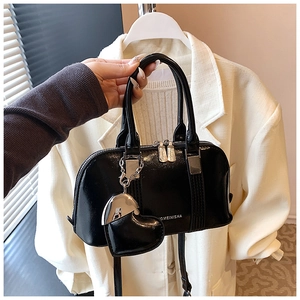 Detail of black glossy handbag featuring heart charm and silver metal hardware accents