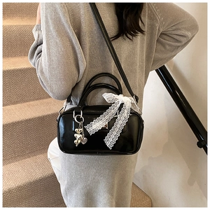 Detail of glossy black bowling bag featuring white lace bow and silver heart pendant