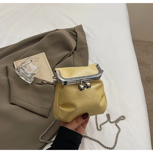 Detail of a mini light yellow crossbody bag with silver chain strap and metal clasp closure