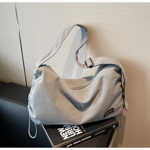 Detail of light grey corduroy crossbody bag featuring a drawstring side and leather logo tag