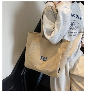 Detail view of large canvas tote bag with side pocket and blue embroidered letters