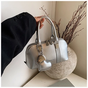 Detail of silver metallic Boston bag featuring a heart-shaped chain pendant and top zipper