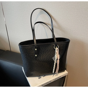 Detail shot of the black leather tote bag featuring a colorful woven rope pendant charm