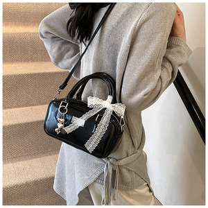 Back view of a black glossy bowling bag with a white lace bow and heart charm on a model