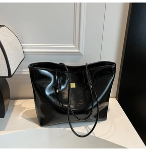 Detail of a black patent leather tote bag with glossy finish and gold metal logo plaque