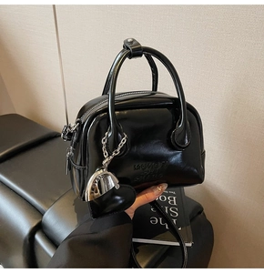 Detail of glossy black Boston bag with silver heart charm and embossed brand lettering