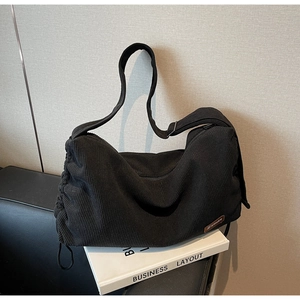 Close-up of black corduroy shoulder bag showing fabric texture and drawstring side detail
