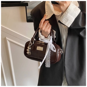 Detail of a dark brown polished leather bowling bag with lace bow and heart charm