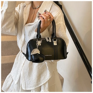 Detail of black Boston shell bag with heart charm and silver hardware on white dress