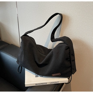 Detail of black corduroy tote bag featuring a leather logo patch and drawstring side design
