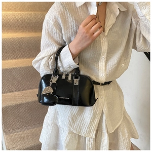 Detail of black glossy shell handbag with heart charm on white textured shirt