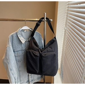 Detail of black nylon tote bag with dual front zipper pockets and wide shoulder strap