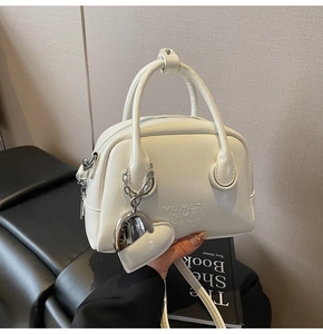 Detail of white leather handbag featuring heart charm and silver chain strap