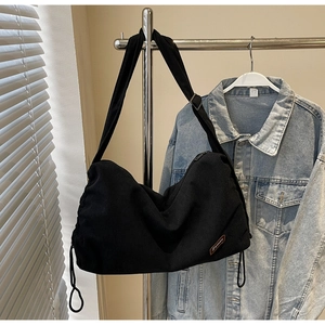 Detail of black corduroy hobo bag with drawstring side and brown leather brand patch