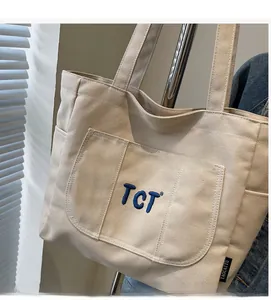 Detailed close-up of beige canvas tote bag with blue TCT embroidery and side brand label