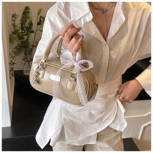 Close-up of beige bowling bag featuring a white lace bow and elegant metal chain charm