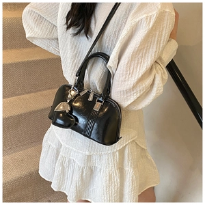 Close-up of black glossy shell bag with heart charm and silver metal hardware details
