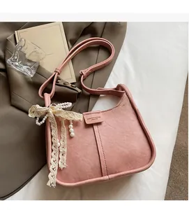 Detail of light pink pebbled leather bucket bag with lace bow and pearl decoration
