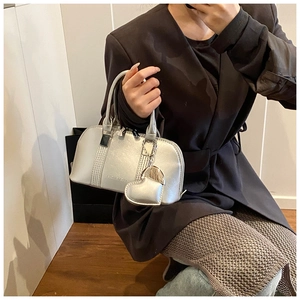 Close-up of a silver metallic Boston bag with a heart charm held by a model in a suit
