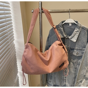 Detail of pink corduroy shoulder bag showing texture, side drawstring and brand logo tag