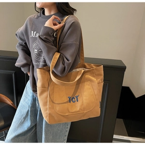 On-shoulder view of khaki canvas tote bag featuring blue TCT embroidery and side pockets