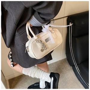 Detail of cream Boston bag featuring lace bow and metal heart charm on synthetic leather