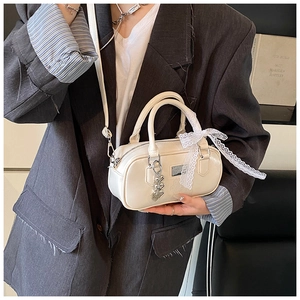 Detail of cream mini bowling bag featuring white lace ribbon and silver heart charm