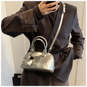 Detail of silver metallic bowling bag with heart charm worn over a dark blazer