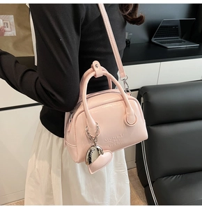 Detail of pink glossy pillow bag with heart pendant and adjustable strap in office setting
