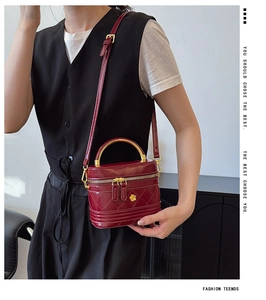 Close-up of burgundy quilted leather box bag with gold handle and flower emblem