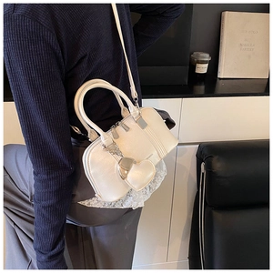 Detail of a creamy white shell-shaped handbag with a heart-shaped charm and long strap