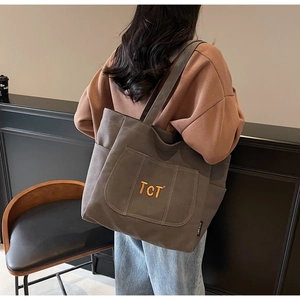 Detail of a large brown canvas tote bag with front pocket and orange embroidered logo