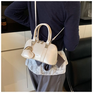 Detailed shot of a pearl white shell crossbody bag featuring a heart pendant and strap