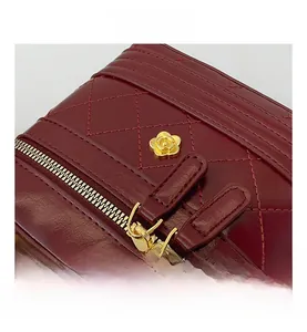 Detail view of deep red quilted leather bag with golden camellia logo and metal zipper